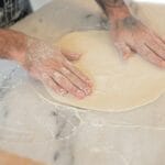 Dłonie zagniatające ciasto na oprószonym mąką blacie kuchennym