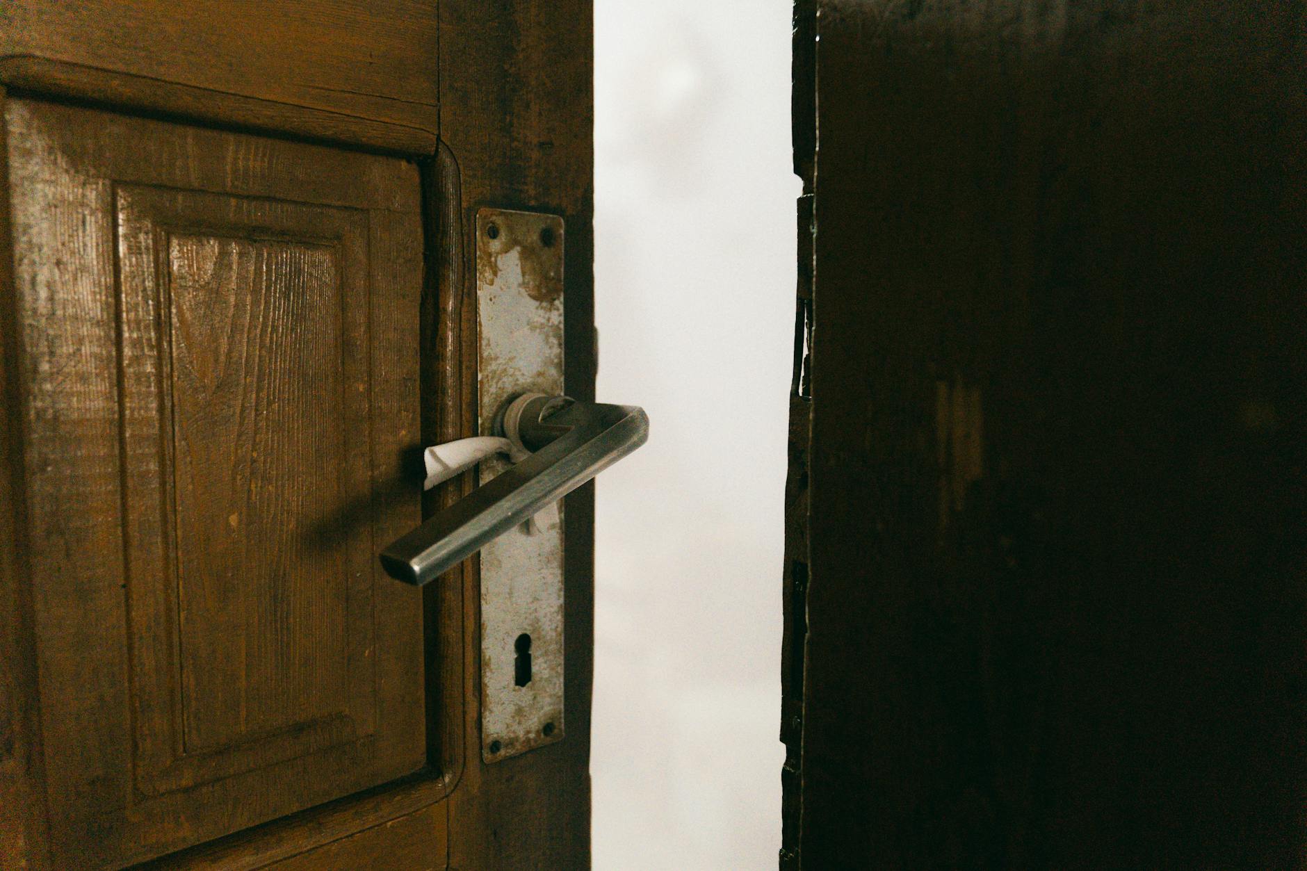 Drewniane, uchylone drzwi z metalową klamką we wnętrzu domu