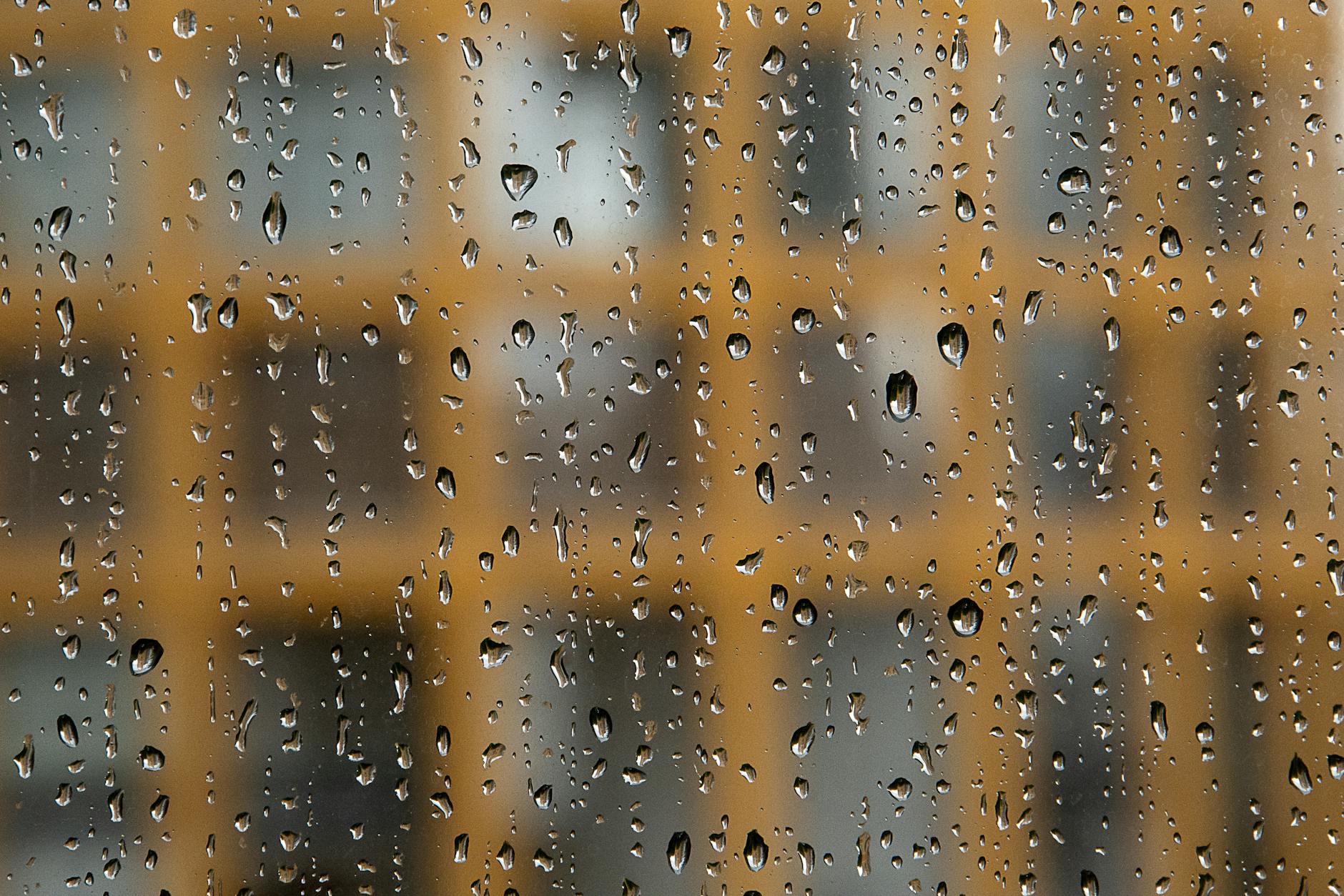 Krople deszczu na szybie okna z rozmytym blokiem w tle