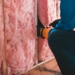 Pracownik montujący różową izolację w ścianie domu energooszczędnego