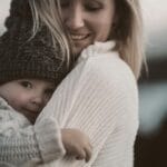 Mama przytula małe dziecko na dworze w ciepłych swetrach