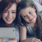 Mama z córką robią sobie radosne selfie na łóżku