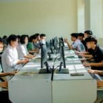Studenci informatyki pracujący zespołowo przy komputerach w sali zajęciowej